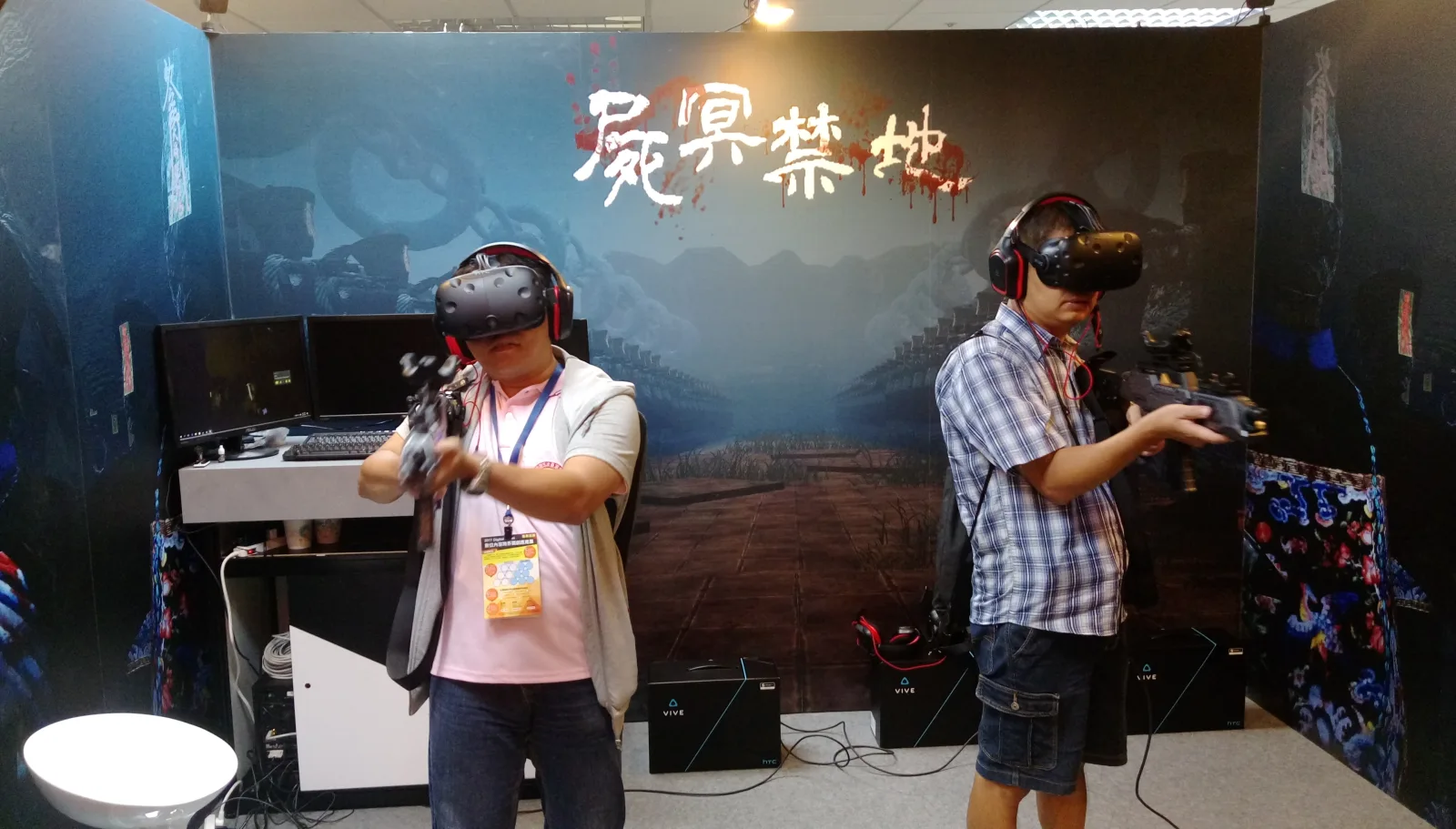 Two players standing in VR headsets and holding physical gun controllers while playing Forbidden Z, in front of a full-height venue wall carrying the game's Chinese title, with tracking base stations on the floor