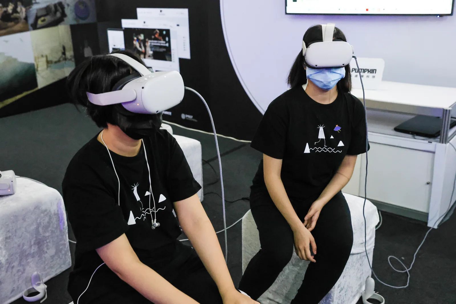 Two visitors seated side by side in Meta Quest 2 headsets trying VR content, with Pumpkin VR's identity on the wall behind them, at Vision Get Wild 2023 in Kaohsiung